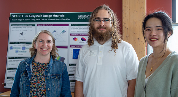 Three people stand in front of a scientific poster.